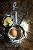 Measuring cups with flour, butter, sugar and an egg