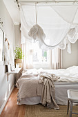 Small, white and grey bedroom with canopy over bed