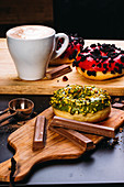 Assorted delicious doughnuts with glaze and toppings composed with chocolate bars and cup of coffee on wooden boards