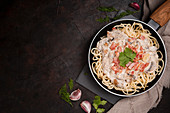 Spaghetti with ham slices and mushrooms in creamy sauce cooked in pan and placed on wooden cutting board