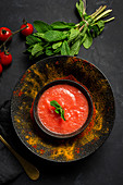 Healthy homemade tomato soup with bread, mint and olive oil on dark background