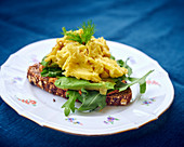 A slice of bread topped with avocado, rocket and scrambled egg