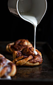 A cinnamon bun on a baking sheet being drizzled with icing