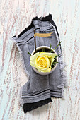 A yellow rose in a small bowl with a denim flag