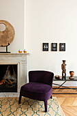 Violetter Sessel vorm offenen Kamin mit Skulptur im Wohnzimmer