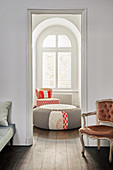 Open doorway leading into living room with ottoman and armchair below arched window