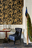 Stuffed peacock on post in seating area with black and gold floral wallpaper