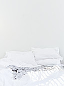 Doppelbett mit weißer Bettwäsche vor weißer Wand