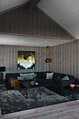 Black corner sofa in dark living room with wood-panelled walls and ceiling