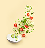 Fresh cut salad ingredients falling into white bowl