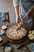 Woman serving apple and frangipane tart with almond flakes