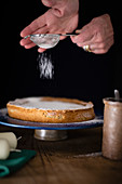 A cake being dusted with icing sugar