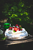 Pavlova mit Erdbeeren und Basilikum auf Tisch im Freien