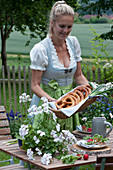 Frau deckt Tisch für die bayrische Brotzeit: Teller mit Radieschen und Brezeln auf Holzscheiben, Bierkrug