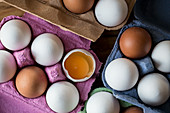 Weiße und braune Eier in Eierkartons, eines aufgeschlagen
