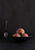 Three scoops of chocolate ice cream in a black bowl