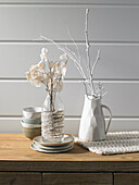 Silver leaf branches in a glass carafe wrapped in woollen threads and white sprayed branches in a jug vase
