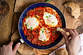 Shakshuka in a pan on an olive wood plate with bread (Tunisia)