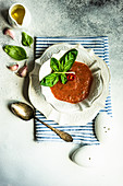 Traditional spanish tomato soup Gazpacho derved in ceranic bowl with fresh basil leaves on stone background with copy space