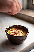 Hand sprinkling paprika on a bowl of homemade organic hummus