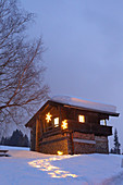 Illuminates snowy path leading to Alpine cabin at dusk