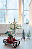 Arrangement of cloth mouse in red toy car and miniature fir tree