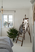 Small Christmas tree next to old stepladder decorated with fur blanket and paper star