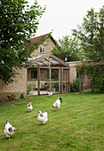 Hühner auf der Wiese vorm Backsteinhaus mit Wintergarten