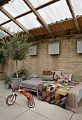 Tricycle, sofa and olive tree in conservatory with brick walls