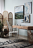 Sprossenstuhl am Holztisch vor hellblauer Wand mit Bildern