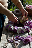 Hands tying wreath of ornamental cabbage leaves and sedums