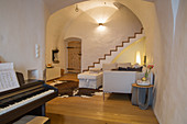 Piano in rustic living room with vaulted ceiling and staircase