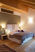 Bed against grey wall in bedroom with wooden ceiling beams
