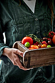 Woman holding wooden box with colorful tomatoes