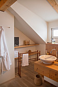 Wooden washstand in modern, country-house-style bathroom with sloping ceiling