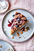 Blueberry coffee cake with pecan streusel dusted with icing powder on a ceramic plate.