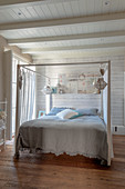 Double, four-poster bed in bedroom with white-painted wooden walls