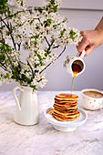 Woman drizzling maple syrup on a stack of pancakes