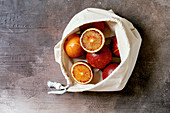 Blood sicilian oranges, ripe and juicy, in cotton eco friendly bag, whole and sliced, over grey concrete background. Flat lay, space