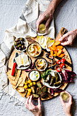 Mediterranean mezze platter with hands selecting food and holding a glass of wine.
