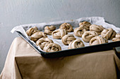 Ready to bake traditional Swedish cardamom sweet buns Kanelbulle on oven tray cover by baking paper on grey linen table cloth.