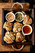 Traditional Swedish cardamom sweet buns Kanelbulle in wooden tray, ingredients sugar, cardamom and syrup in ceramic bowl on wooden table. Flat lay, space