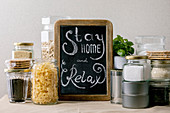 Kreidetafel mit der Aufschrift 'Stay home and relax' inmitten von Lebensmittelvorräten