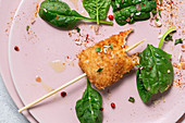 Chicken skewers in batter fried in fried panko on restaurant table with tomato concentrate, soy sauce, mustard sauce, spices and spinach Oriental food