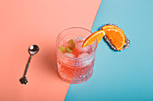 Top view of alcohol cocktail with ice cubes and sprig of mint in glass placed on colorful background with orange slices