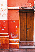 Rote Hauswand mit Holztüre und abgeblätterter Farbe
