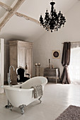 Freestanding bath in room with french drawers, silver carved French chair and black chandelier