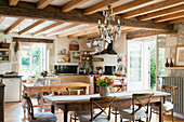 Rustic kitchen with French wooden dining table, ceilings beams, glass chandelier and traditional Camargue-style dining chairs