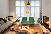 Langes Polstersofa, grüne Sessel und Kamin im Wohnzimmer