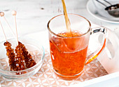 Tee in eine Glastasse giessen und mit Kandisstange umrühren